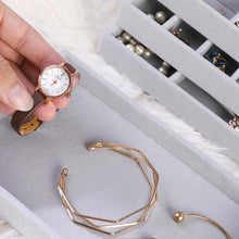 Load image into Gallery viewer, Close-up of a hand placing a vintage brown leather strap wristwatch into a gray velvet jewelry tray. The compartment also holds minimalist gold bracelets, emphasizing an organized and elegant storage solution. Ideal for preserving and showcasing watches, bracelets, and other accessories in a luxurious manner.