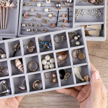 Load image into Gallery viewer, Hands showcasing an elegant gray velvet jewelry tray filled with neatly organized accessories, including pearl earrings, gold rings, delicate chains, and stylish brooches. The tray's grid design ensures secure and tidy storage, perfect for displaying jewelry collections in a sophisticated and practical way.