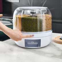 Laden Sie das Bild in den Galerie-Viewer, Hand pressing a button on a rotating grain dispenser, which has multiple clear compartments filled with grains like millet, mung beans, and rice. The dispenser's design allows for easy, controlled access to stored grains, making it a convenient kitchen storage solution.
